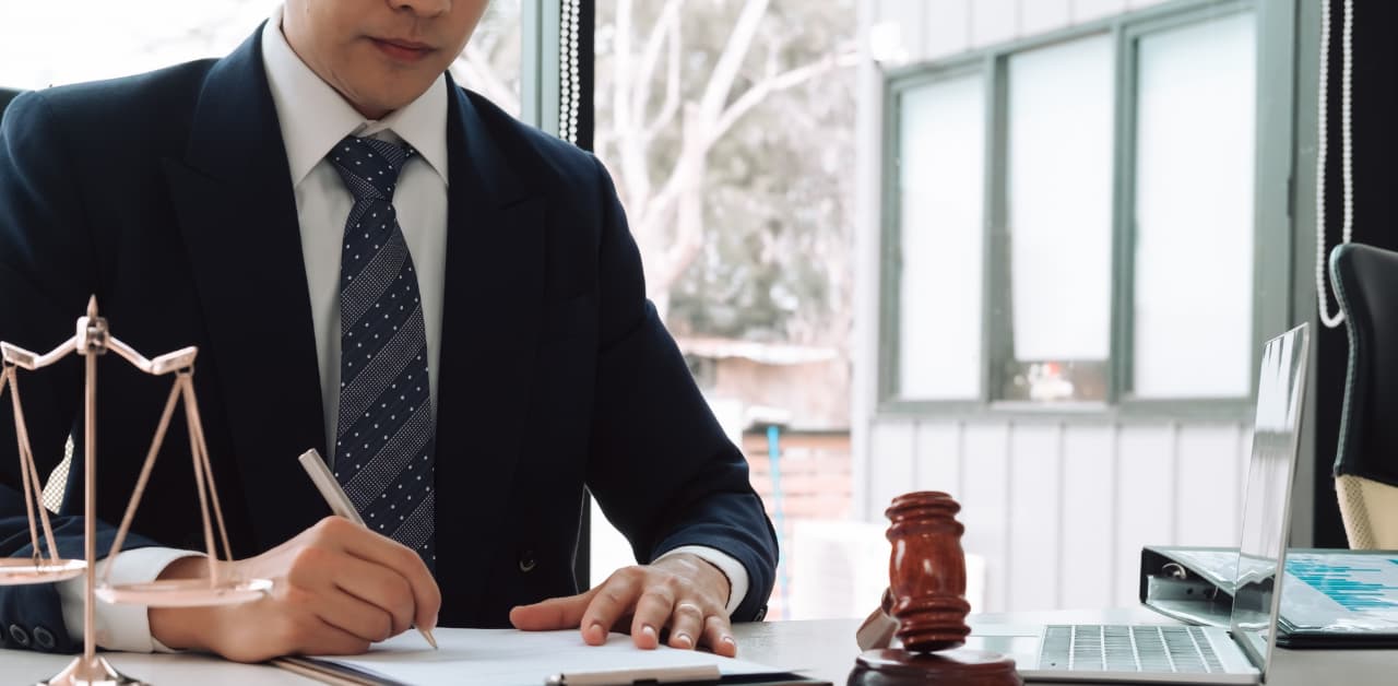 Lawyer in a suit writing at a desk beside a gavel and scales of justice